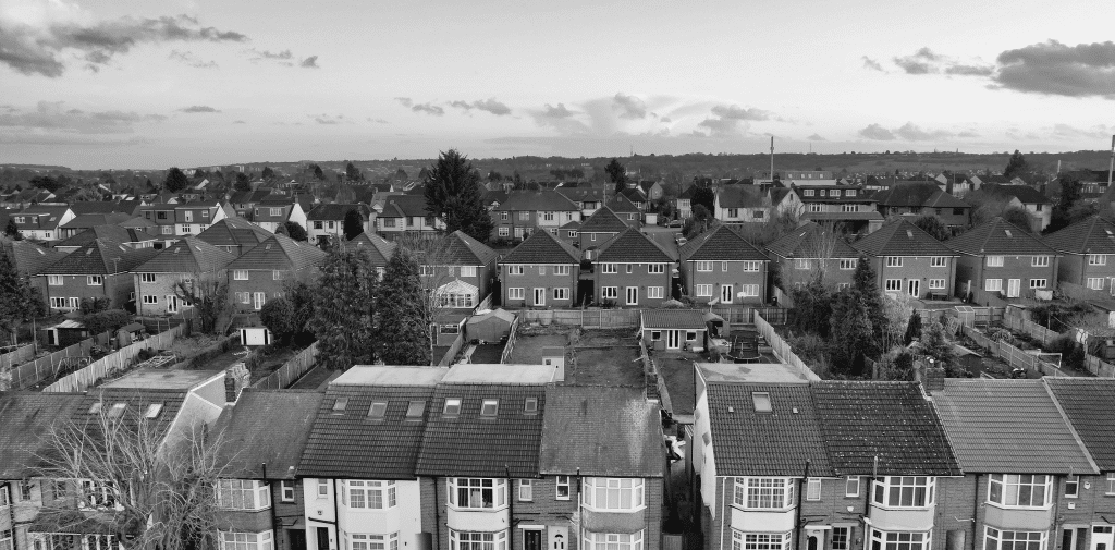 Monochrome aerial view of a dense suburban neighborhood with rows of tiled-roof houses and backyards.